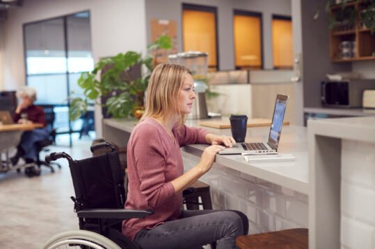 Woman in wheelchair working on a laptop at a modern cafe counter.