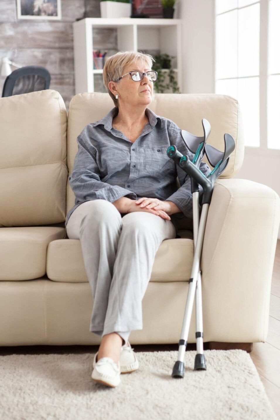 Senior woman with crutches sitting on sofa, promoting benefits of walking aids and mobility support.