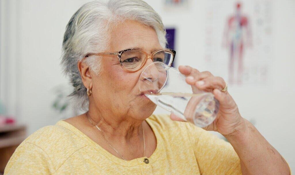 Elderly woman drinking water to stay hydrated for muscle health and balance.