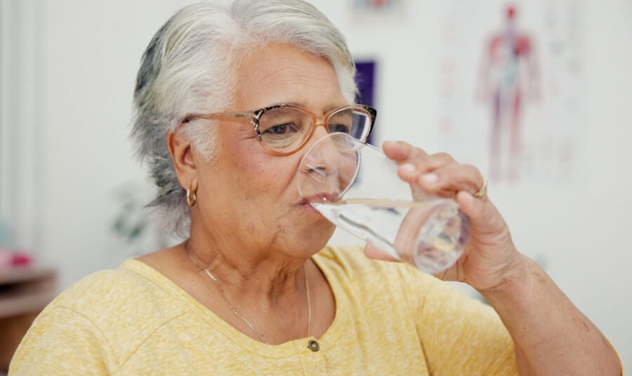 Elderly woman drinking water to stay hydrated for muscle health and balance.
