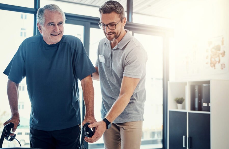 Elderly man walking with support from caregiver in a bright, modern indoor setting.