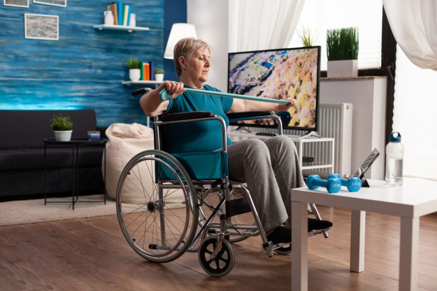 Elderly woman in wheelchair doing seated exercise with a stick at home.